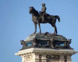 There is a statue of the monarch riding a horse situated on a tall central core.